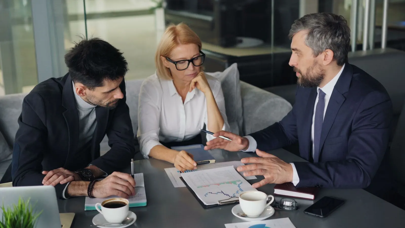 Three colleagues reviewing printed charts together beside an open laptop.