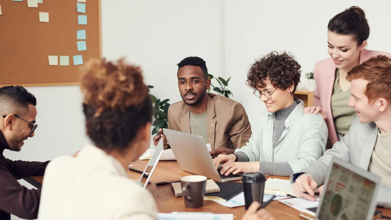 A team compares documents and laptop information during a shared office discussion.