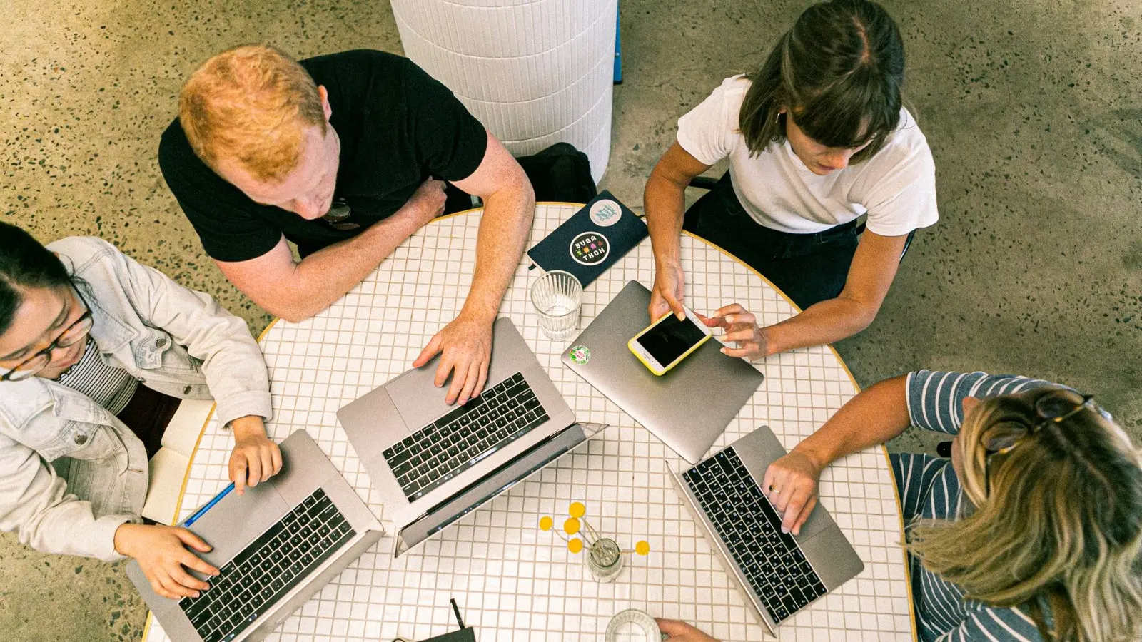 Overhead view of colleagues comparing laptops, notes, and a phone at a shared desk.