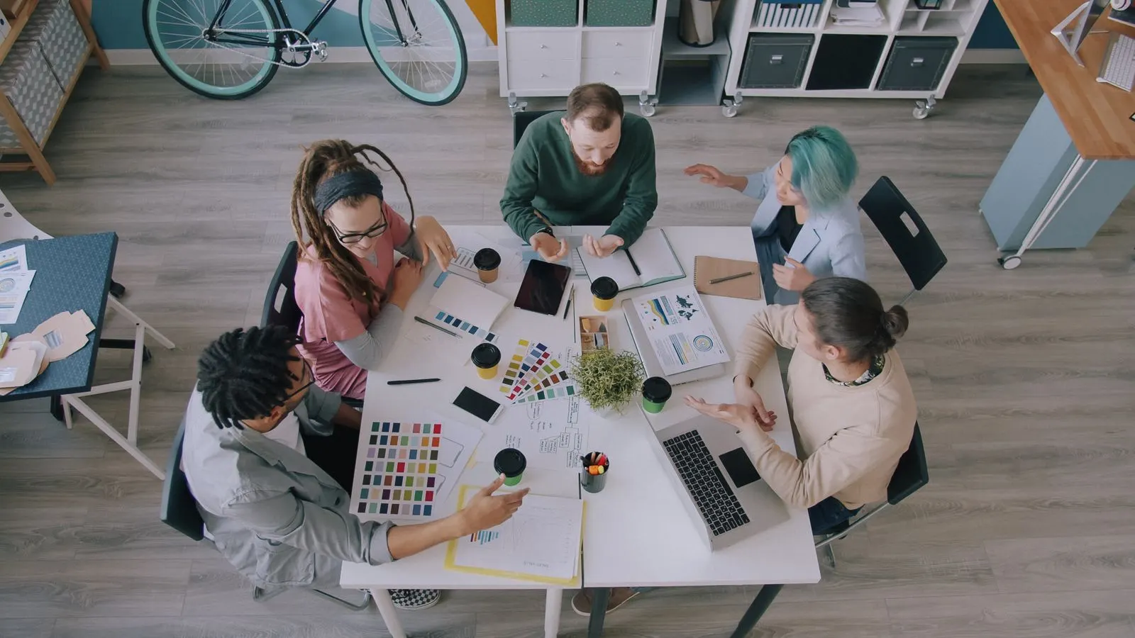 Overhead view of a team comparing color swatches, notes, and laptops at a shared table.