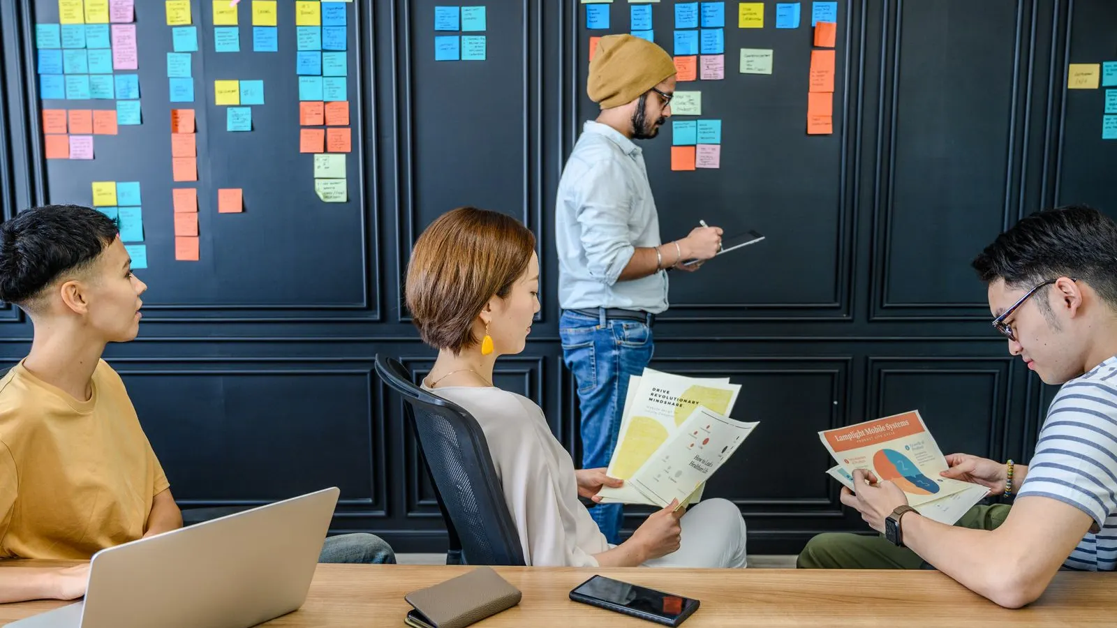 A team discussing a wall of colorful sticky notes beside their laptops.