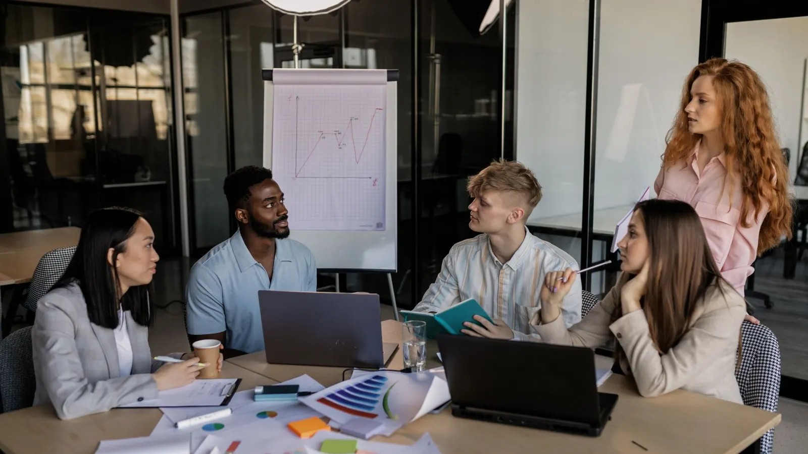 Colleagues discussing printed charts and an open laptop at a shared table.