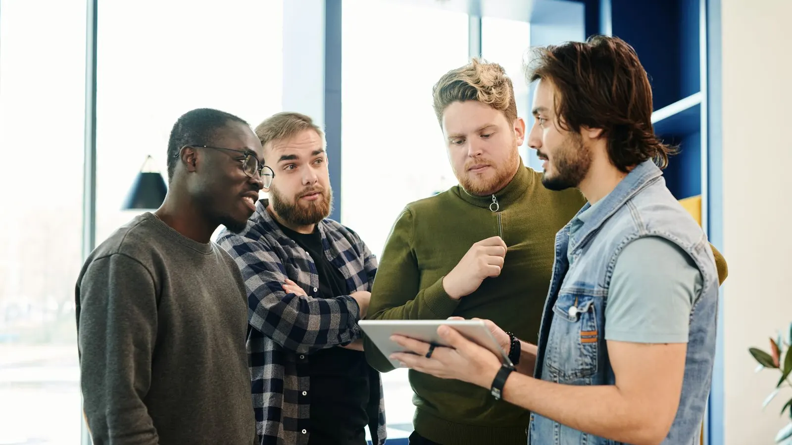 Four colleagues gathered around a tablet during a standing office discussion.